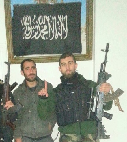 Özgür Deveci som jihadist med al-Qaeda flag i baggrunden, Syrien/Tyrkiet (2013). 